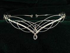 Stunningly beautiful handmade silver plated elven circlet crafted from just three lengths of wire to emulate traditional Celtic knotwork.  Designed to be worn on the forehead, the circlet is open at the back with loops for ribbon or cords to be attached enabling the circlet to be held in place. It can also be pinned into place if preferred. The circlet is flexible and very comfortable to wear. The design of the circlet measures approx 32cms (12 and a half inches) across and 3cms (1 and a quarter inch) from top to bottom at the centre. The full circumference of the circlet is 53cms (20.5 inches). Designed and made in the beautiful English County of Kent. Shipping is via Royal Mail First Class Delivery for UK orders and Tracked Airmail for overseas deliveries. Wedding Circlet, Elven Circlet, Bridal Circlet, Wedding Handfasting, Boho Bridal Headpiece, Pagan Wedding, Boho Headpiece, Tiara Headpieces, Medieval Wedding