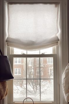 a window with a white roman blind in front of it and a black purse on the windowsill