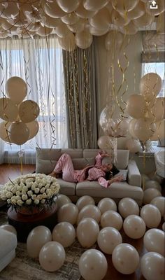 a living room filled with lots of balloons and white flowers on top of a wooden floor