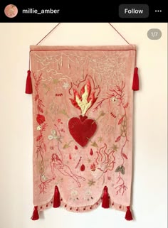 a pink wall hanging with red tassels and a heart shaped decoration on it