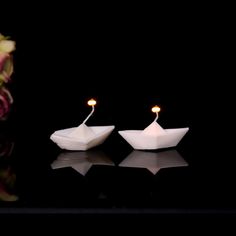 two small white boats sitting next to each other on a black surface with flowers in the background