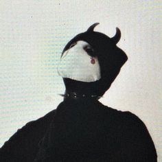 a person wearing a black and white mask with horns on their head is standing in front of a wall