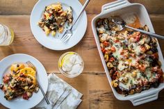 a casserole dish filled with pasta and vegetables next to two glasses of water