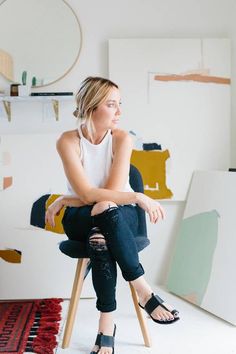 a woman is sitting on a chair in front of some paintings and looking off into the distance