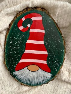 a green and red painted wood slice with a gnome's hat on it, sitting on a white blanket