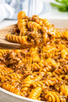 a wooden spoon full of macaroni and cheese being lifted from a large pot