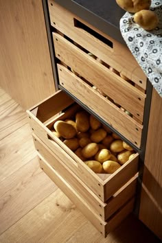 a wooden box filled with potatoes sitting on top of a floor next to a counter