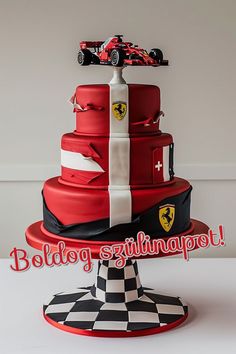 a red and white cake with cars on top is sitting on a pedestal in front of a wall