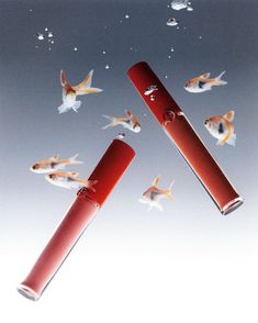 two red lipstick tubes floating in the air with goldfish flying around them on a blue sky background