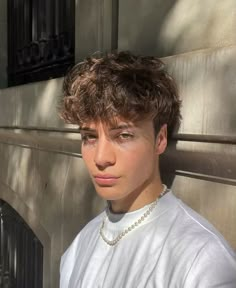 a young man standing next to a wall wearing a white shirt and pearls on his necklace