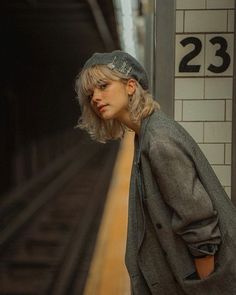 a woman standing in front of a train station next to a loading platform with her hand on her hip