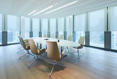 an empty conference room with chairs and a table in the foreground is large windows