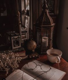 an open book with glasses on it next to a cup of coffee and a lantern