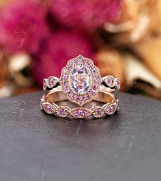 two wedding rings with pink and white diamonds on top of a table next to flowers