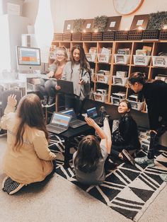 a group of people sitting on the floor in front of laptops and bookshelves