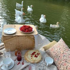 a picnic table with food and drinks on it in front of the water, swans