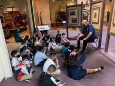 a man standing in front of a group of children sitting on the floor next to each other