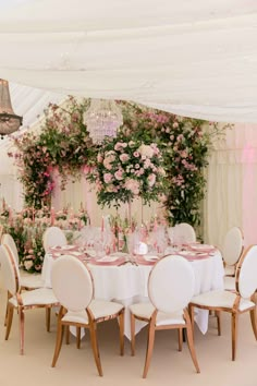 a table set up with white chairs and pink flowers