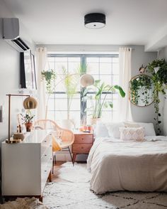 a bedroom with white bedding and plants on the window sill in front of it