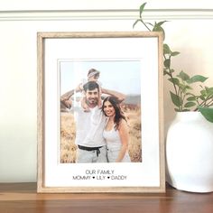 a wooden frame with a family picture on it next to a potted plant and a white vase