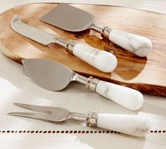 three silver and white utensils sitting on top of a wooden tray next to each other