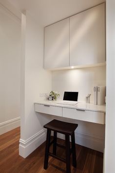 a white desk with a laptop on top of it in front of a wall mounted cabinet