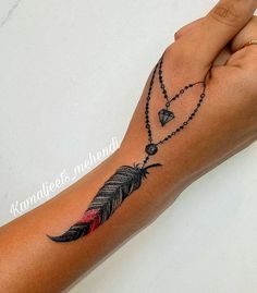 a woman's arm with a black and red feather tattoo on the left wrist