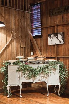 an old dresser is adorned with greenery in the corner of a rustic barn - like room