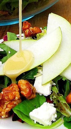 a salad with dressing being drizzled onto it's side, on a plate