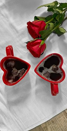 two red heart shaped vases sitting on top of a table next to a rose