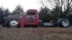 an old red truck parked on top of a dry grass field next to some trees