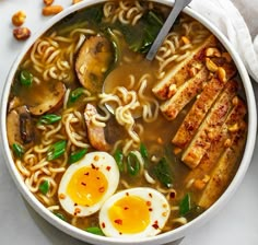 a bowl of ramen with noodles, eggs and spinach in it on a white surface