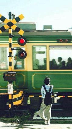 a woman walking down the street in front of a green and yellow train passing by