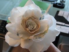 a hand holding a white flower on top of a table next to a computer keyboard