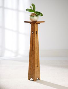 a small wooden table with a plant on it's top and two bells at the base