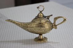 an ornate brass teapot with arabic writing on the lid sits on a white surface