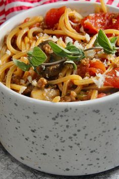 a white bowl filled with pasta and sauce on top of a tablecloth next to a fork