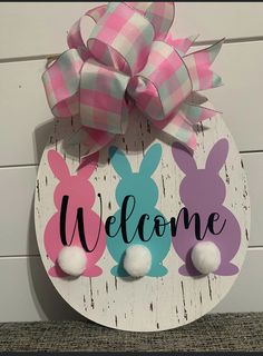 a welcome sign with two bunny ears and a bow on the top, sitting against a white wall