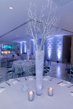 a tall vase filled with white flowers sitting on top of a table next to candles