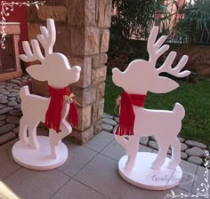 two white wooden reindeer statues with red scarfs on their heads and antlers in front of a brick wall