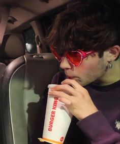 a man wearing sunglasses and drinking from a cup in the back seat of a car