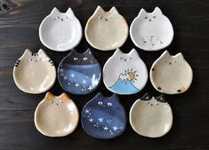 nine ceramic bowls with cats painted on them are arranged in a circle and placed on a wooden surface