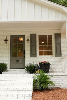 a white house with green shutters and potted plants on the front steps outside