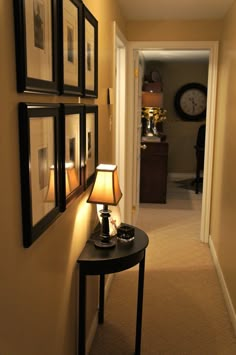 a hallway with pictures on the wall and a lamp next to it, in front of a clock