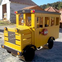 a small yellow toy train sitting on top of a gravel road next to a building