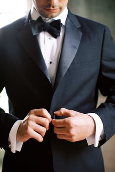 a man in a tuxedo adjusts his bow tie