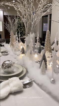 the table is set with silver and white christmas trees, candles, and plates on it