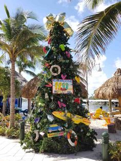 a decorated christmas tree on the beach with surfboards all over it and decorations hanging from palm trees