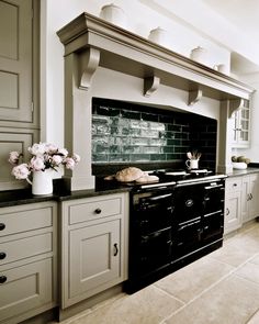 a black and white photo of a kitchen with an oven, range hood, cabinets, and flowers on the counter