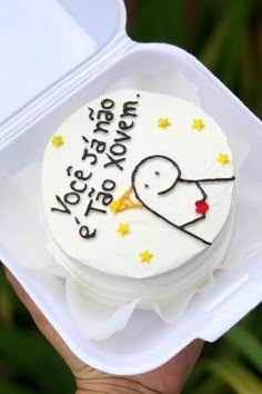 a person holding up a small cake in a plastic container with writing on the side